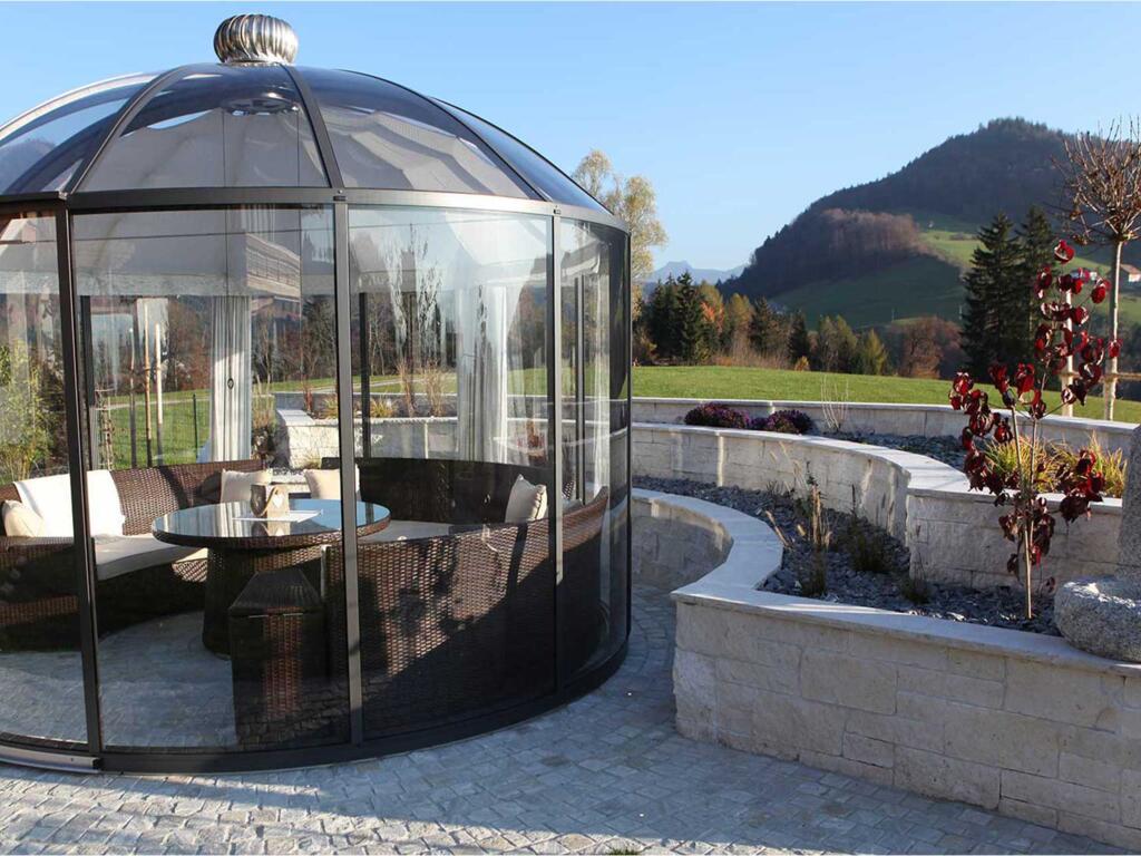Glaspavillon umrundet von Gartenmauer mit Pflanzzonen und Brunnen